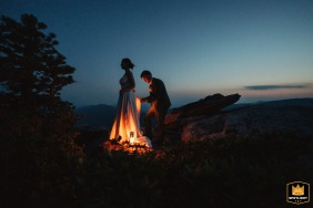 The groom helps his wife with her wedding dress at dusk before they descend the summit of Hawksbill Mountain, North Carolina